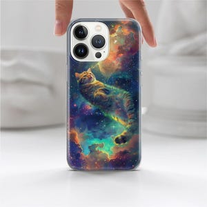 May include: A clear phone case featuring a colorful galaxy design with a tabby cat floating in space. The case has a glossy finish and is held by a hand.