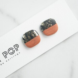 May include: Square stud earrings with a two-tone design. The top half is black with gold flecks, and the bottom half is a terracotta color. The earrings are displayed on a white card with the text "POP" and "made earrings".