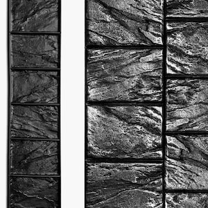 May include: Black and gray textured stone panels. The panels have a rough, uneven surface, with a dark, almost black color. The design is reminiscent of natural stone, with visible lines and variations in texture. The panels are arranged in a rectangular pattern.