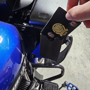 Puede incluir: Una tarjeta de certificación PADI 50 years negra y rectangular con un logotipo de globo terráqueo dorado y texto. La tarjeta se sostiene contra un marco de motocicleta azul con una defensa negra y un reposapiés de metal azul visible abajo.