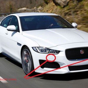 May include: A white Jaguar sedan driving on a winding road. The car has a black grille and black trim around the windows. The car is in motion and the wheels are turning.