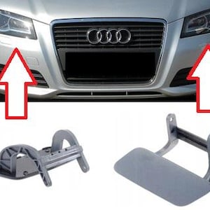 Könnte beinhalten: Zwei graue Scheinwerferwaschabdeckungen und eine Scheinwerferwaschdüse werden vor einer silbernen Stoßstange eines Autos gezeigt. Die Abdeckungen sind rechteckig und die Düse hat ein gebogenes Design. Die Stoßstange des Autos hat einen schwarzen Kühlergrill und das Audi-Logo.
