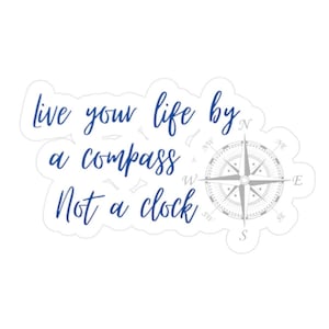 May include: White sticker with blue text that reads "live your life by a compass Not a clock." A gray compass rose graphic is on the right side of the sticker. The sticker has a white border.