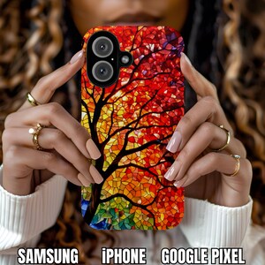 May include: A colorful phone case featuring a stained-glass tree design with red, orange, yellow, and green hues. The case has a black camera module and the words "SAMSUNG", "iPHONE", and "GOOGLE PIXEL" at the bottom.
