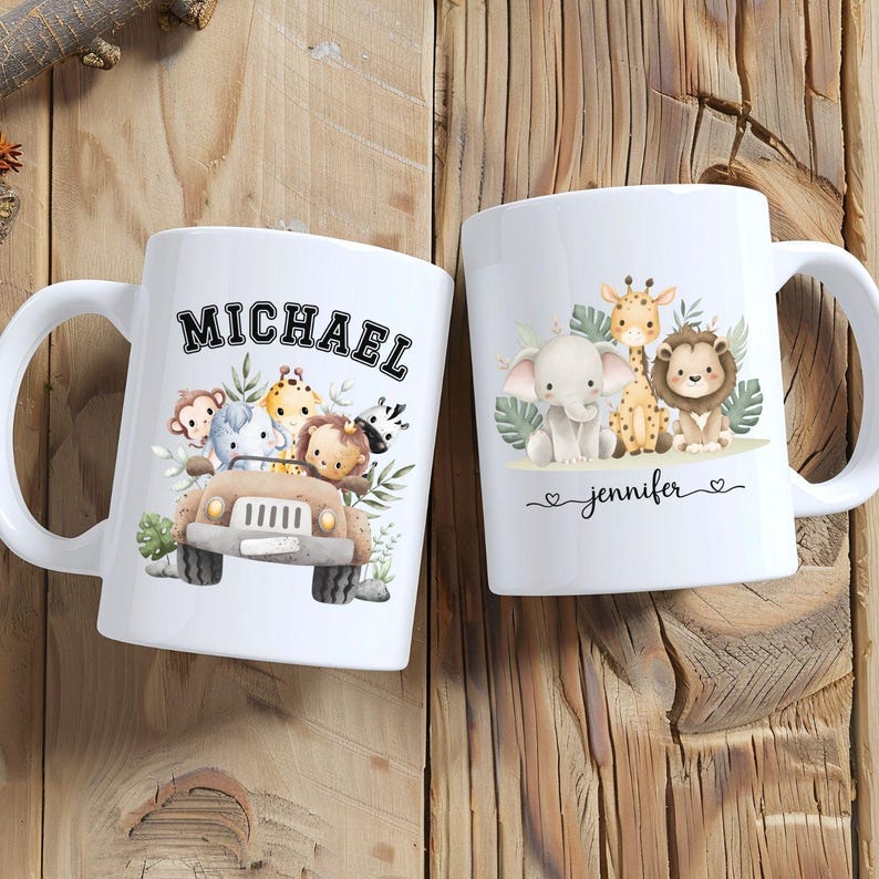 May include: Two white ceramic mugs with safari animal illustrations. One mug features a jeep with animals and the name "MICHAEL". The other mug has an elephant, giraffe, and lion with the name "jennifer".