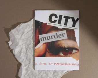 Pode incluir: Um fanzine intitulado "CITY murder" com uma capa em estilo de colagem com um close-up de um olho. O fanzine está em um pedaço de papel branco amassado contra um fundo marrom. O texto "A ZINE BY MADDIESMERCANTILE" também é visível.