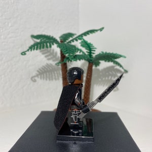 Op de afbeelding: Een zwart Lego minifiguur met een zwarte cape en een zilveren zwaard. Het minifiguur staat op een zwarte basis.
