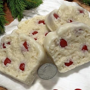 May include: Four white chocolate covered loaf cakes with red candy pieces inside. The cakes are on a white surface with a quarter next to them.