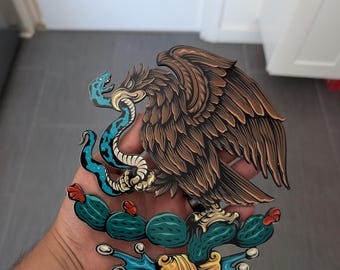 May include: A detailed illustration of an eagle with outstretched wings, a snake in its beak, and a cactus. The eagle has brown feathers, the snake is blue, and the cactus is green with red accents. The design is a symbol of national pride.