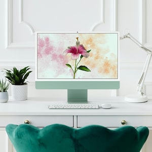 May include: A computer monitor displaying a digital illustration of a pink hibiscus flower on a watercolor background. The monitor is on a white desk with a keyboard and a lamp.