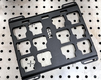 May include: A rectangular black metal panel featuring a grid of twelve square cutouts and four elongated mounting slots at the corners. The word custom is vertically embossed in the center of the panel between the middle column of cutouts.