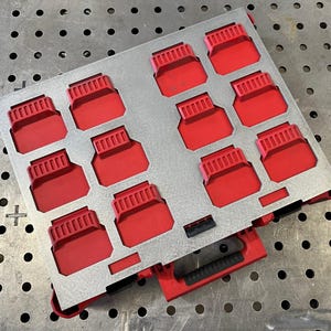 May include: A metal tray with a grid of red compartments. Each compartment has a rectangular shape with a ridged top. The tray is silver and has a red base with a black handle.