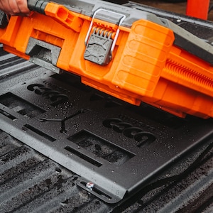 May include: An orange and gray toolbox with a black mounting plate. The toolbox has a handle and a latch. The mounting plate has cutouts and the word "CGCG" etched into it. The items are on a textured surface.