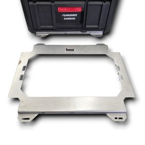 May include: A rectangular silver metal mounting bracket with a central cutout and integrated side slots, featuring the text "boco" printed in black on the top edge, positioned in front of a black Husky Build-Out storage case with a red latch.
