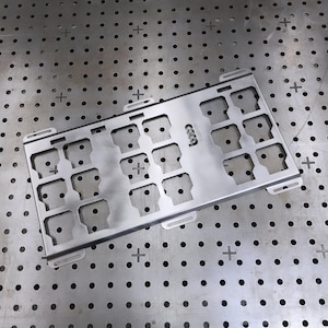 Peut inclure: Un panneau rectangulaire en métal argenté présentant une grille de douze fentes rectangulaires découpées, disposées en trois colonnes. Le mot custom est gravé verticalement au centre. Le panneau comporte quatre pattes de fixation.