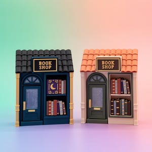 May include: Two miniature book shop models. One is navy blue with a black roof, the other is peach with an orange roof. Each has a sign that reads "BOOK SHOP". The shelves are filled with miniature books.