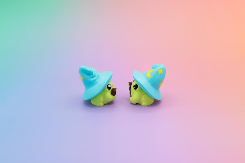May include: Two small, green, cartoon-like figures wearing light blue wizard hats with yellow crescent moons and stars. The figures have brown noses and are set against a gradient background of purple, pink, and green.