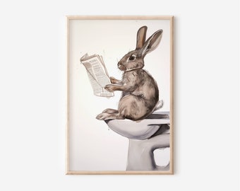 May include: Watercolor print of a brown rabbit sitting on a toilet, reading a newspaper. The artwork is framed in a light wood frame. The rabbit is the focal point, with the toilet and newspaper providing context.
