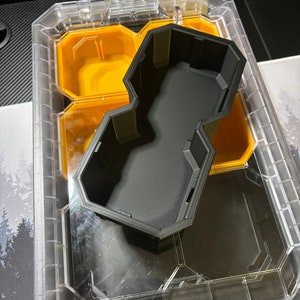 以下が含まれることがあります： 六角形の黒いプラスチック製のオーガナイザーインサートは、透明なプラスチック製の収納ボックスに収まります。インサートには複数のコンパートメントがあります。