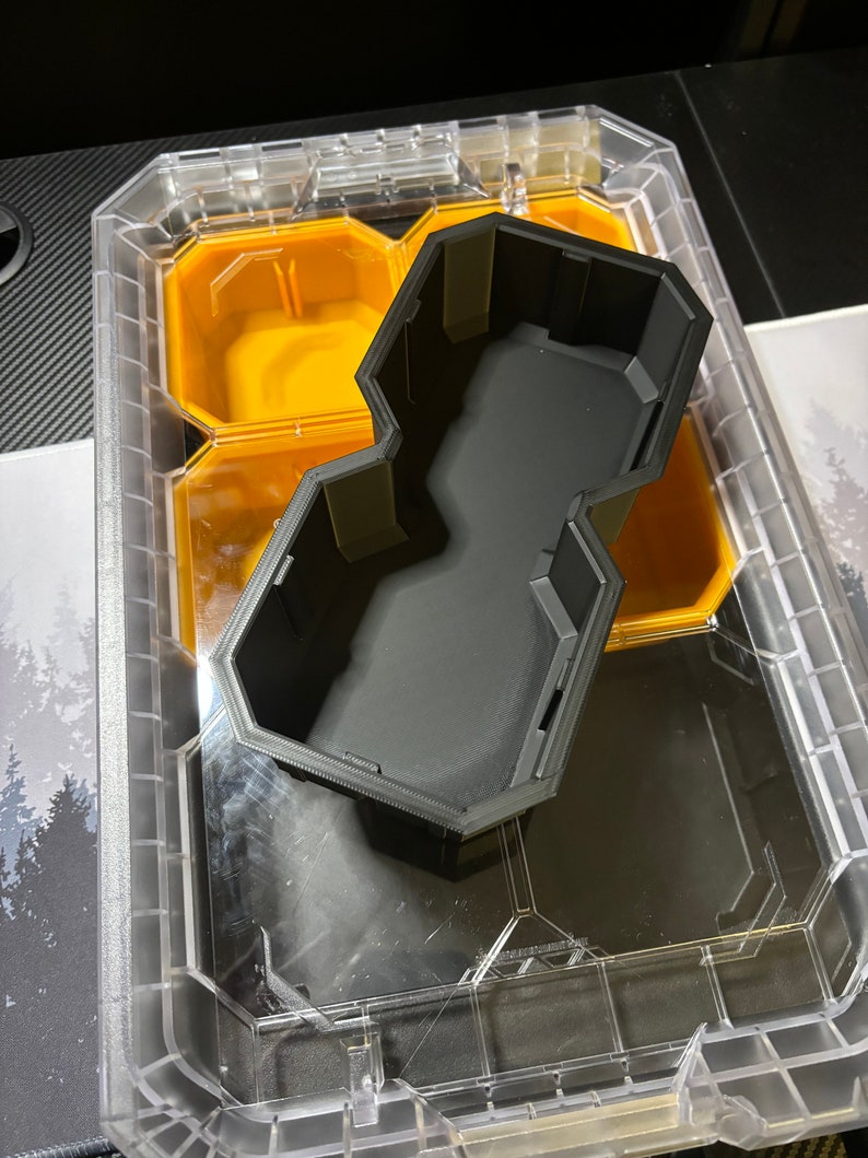 以下が含まれることがあります： 六角形の黒いプラスチック製のオーガナイザーインサートは、透明なプラスチック製の収納ボックスに収まります。インサートには複数のコンパートメントがあります。
