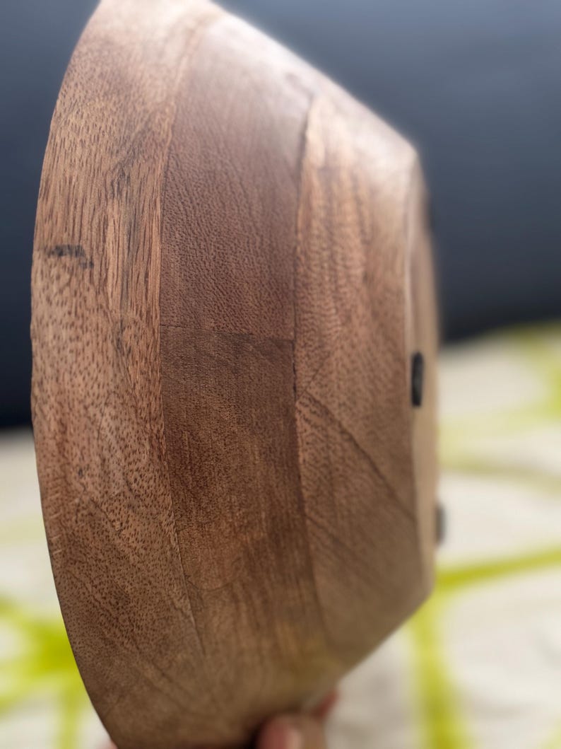 Op de afbeelding: Een houten kom met een natuurlijke, warme bruine kleur. De kom heeft een glad, gebogen ontwerp en een zichtbare houtnerftextuur. De kom wordt waarschijnlijk gebruikt om voedsel in te serveren of als decoratief stuk.