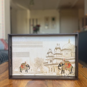 Könnte beinhalten: Ein rechteckiges Serviertablett aus dunkelbraunem Holz mit einem hellen Boden, das eine detaillierte Illustration eines großen Kuppelgebäudes und zweier Elefanten mit bunten dekorativen Decken und Kopfschmuck vor einer Landschaft zeigt.