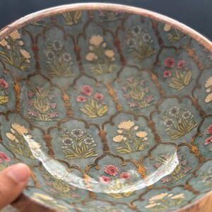 Op de afbeelding: Een decoratieve kom met een turquoise interieur met een bloemenpatroon in roze, geel en wit. De rand is van natuurlijk hout. Het ontwerp van de kom bevat een ingewikkeld, zich herhalend boogmotief. Diameter ongeveer 20 cm.