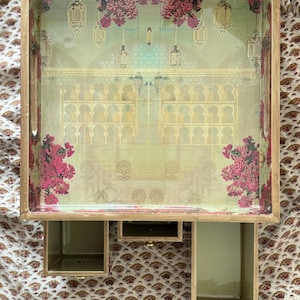 May include: A wooden tray with a decorative design featuring a floral pattern and intricate details. The tray has three compartments for storage.