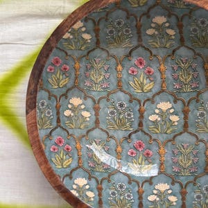 Op de afbeelding: Een ronde houten kom met een turquoise interieur met een bloemenpatroon in roze, wit en geel. De rand van de kom is gemaakt van donkerbruin hout en het ontwerp heeft een sierlijke, vintage uitstraling.