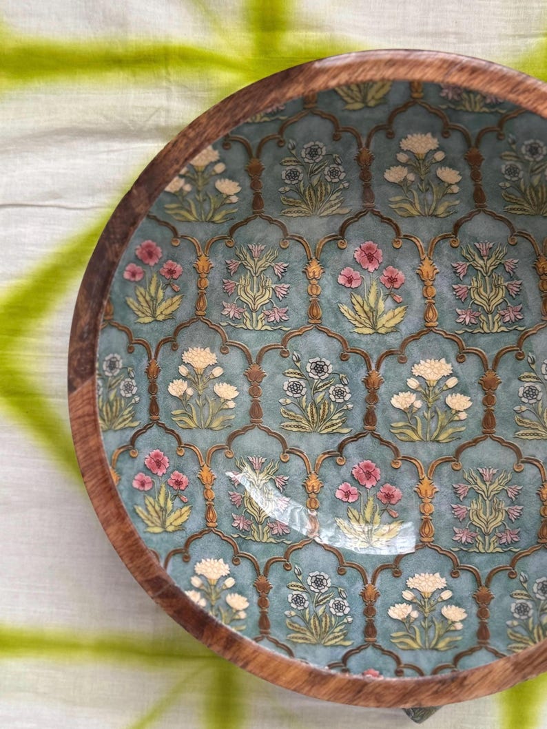 Op de afbeelding: Een ronde houten kom met een turquoise interieur met een bloemenpatroon in roze, wit en geel. De rand van de kom is gemaakt van donkerbruin hout en het ontwerp heeft een sierlijke, vintage uitstraling.