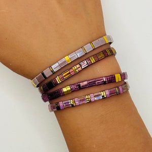 Peut inclure: Quatre bracelets empilés avec un motif géométrique de carreaux violets, dorés et argentés.