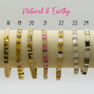 May include: Twelve bracelets made of small tiles in various natural colours and patterns, including gold, white, black, brown, and pink. The bracelets are arranged in a row on a beige surface. The text "Natural & Earthy" is displayed above the bracelets.