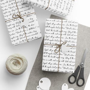 May include: Several wrapped gifts with white paper printed with black script, tied with twine and tags. A ball of twine, scissors, and blank tags are also on the white and gray surface. The gifts are ready for the holidays.