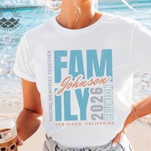 May include: White t-shirt featuring the word "FAMILY" in blue block letters, the name "Johnson" in a cursive font, and the year "2026" in grey. The shirt also says "REUNION" and "SAN DIEGO, CALIFORNIA".