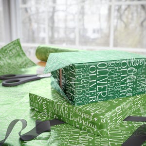 May include: Green gift boxes wrapped in matching paper with the name "Oliver" and "Happy Birthday" printed in white. A pair of scissors, ribbon, and wrapping paper are also visible.