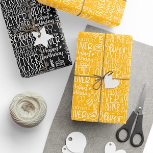 May include: Gift-wrapped presents with personalized "Oliver" birthday wrapping paper in black and yellow. The gifts are tied with twine and adorned with star and heart-shaped tags. A spool of twine, scissors, and blank tags are also visible.