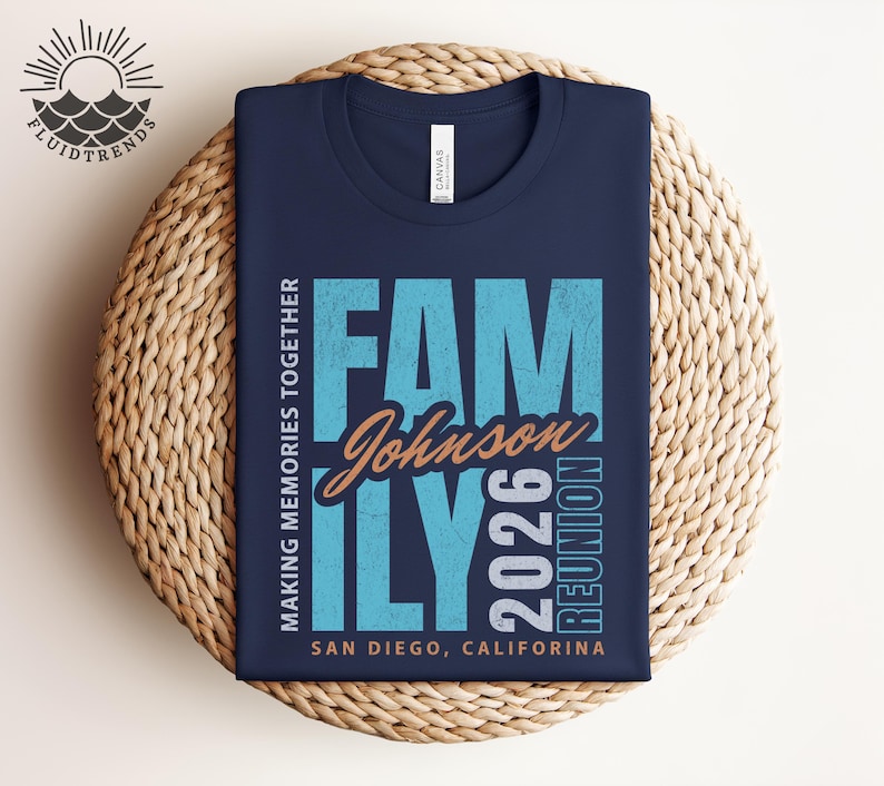 May include: A navy blue t-shirt featuring a teal and orange graphic that reads "FAMILY Johnson 2026 REUNION" and "MAKING MEMORIES TOGETHER" with "SAN DIEGO, CALIFORNIA" at the bottom. The shirt is folded on a woven surface.