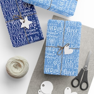 May include: Several wrapped gifts with blue and white patterned paper, featuring the name "Oliver" and the words "Happy Birthday." The gifts are tied with twine and adorned with white tags. A ball of twine, scissors, and blank tags are also present.