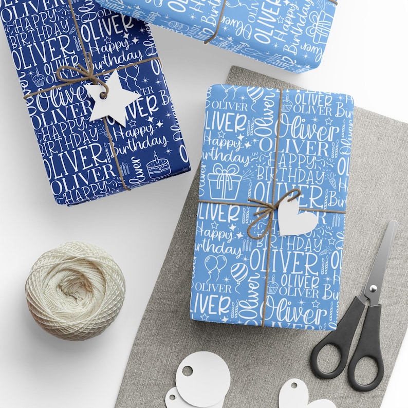 May include: Several wrapped gifts with blue and white patterned paper, featuring the name "Oliver" and the words "Happy Birthday." The gifts are tied with twine and adorned with white tags. A ball of twine, scissors, and blank tags are also present.