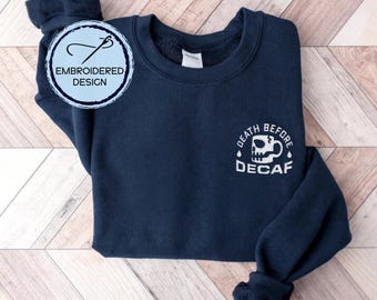 May include: Navy blue sweatshirt with white embroidered text that reads "Death Before Decaf" and a skull and crossbones coffee cup graphic.