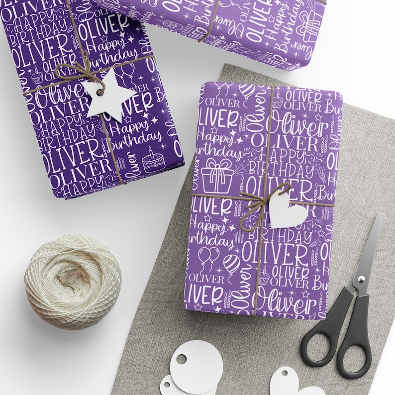 May include: Purple gift wrap with the name "Oliver" and "Happy Birthday" in white. The wrapping paper is decorated with gift boxes, balloons, and cake illustrations. The gifts are tied with twine and adorned with white star and heart-shaped tags.