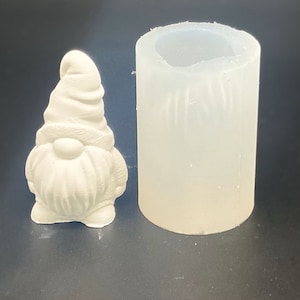 Könnte beinhalten: Eine weiße Keramik-Gnomfigur mit spitzem Hut und Bart, neben einer klaren Silikonform.