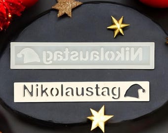 May include: Two white rectangular signs with the text "Nikolaustag" in black lettering. The signs are on a black surface with red and gold glitter stars.