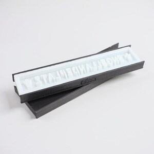 Könnte beinhalten: Eine schwarze rechteckige Form mit dem Text "W STAJO SMAJOW" in weißen Buchstaben. Die Form ist geöffnet und zeigt das weiße Innere. Die Form liegt auf einer schwarzen Oberfläche.