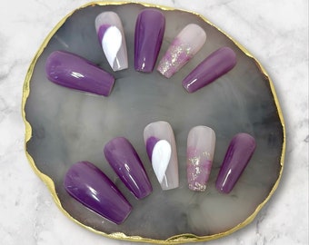 Op de afbeelding: Set van tien paarse en witte kistvormige press-on nagels met een wit hartontwerp op sommige nagels. De nagels worden gepresenteerd op een grijs en gouden steenachtig oppervlak.