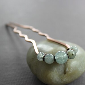 May include: A copper hair pin with a wavy design and a row of light blue gemstone beads.