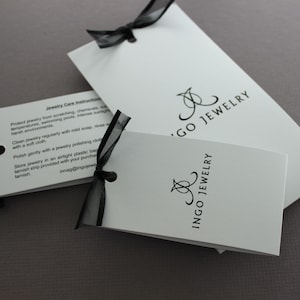 May include: White card with black text and a black ribbon. The text on the card reads "Jewelry Care Instructions" and "Ingo Jewelry".