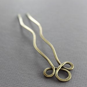 May include: A pair of gold hair pins with a wavy design and a double loop at the end.