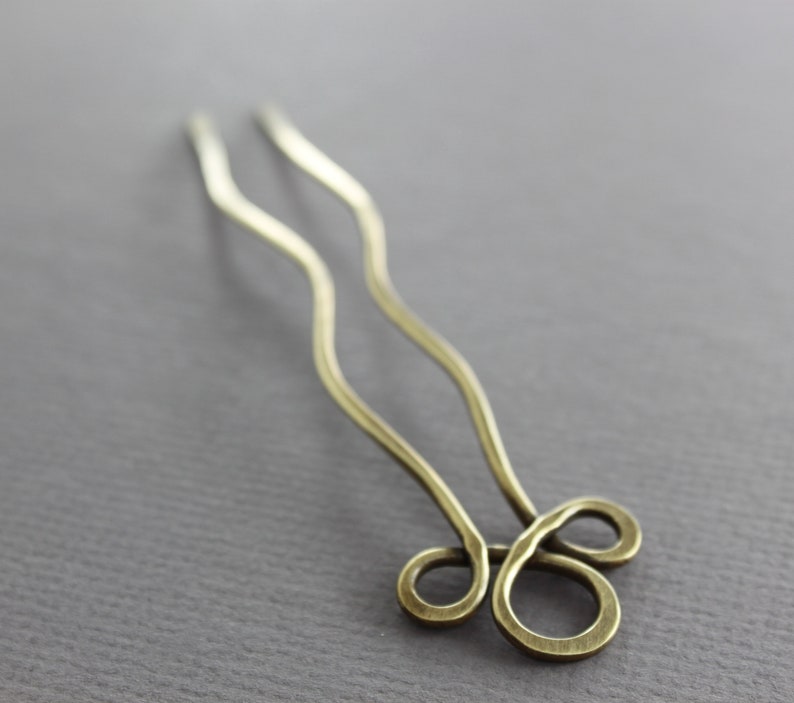 May include: A pair of gold hair pins with a wavy design and a double loop at the end.