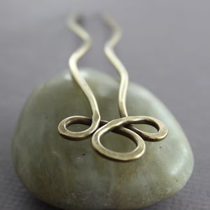 May include: A brass hair pin with a simple, elegant design. The pin is shaped like a figure eight and has a smooth, polished finish.